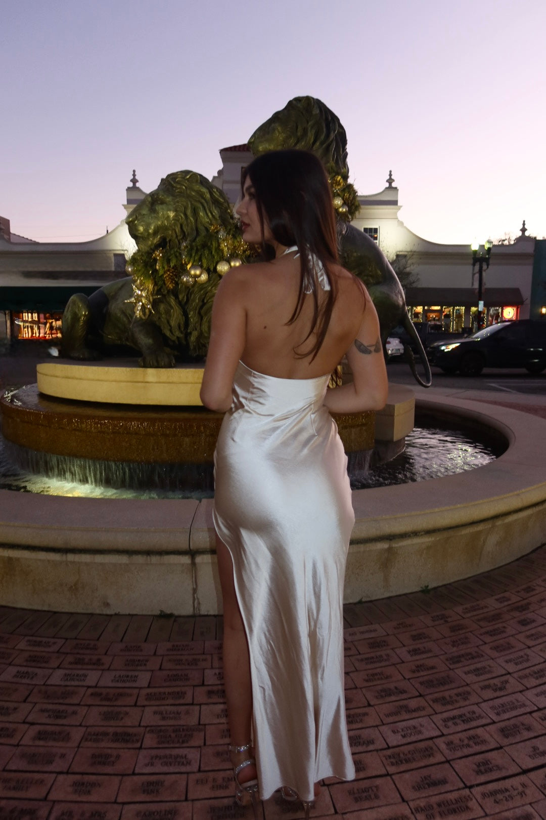 Woman in a white dress standing by a fountain at night.
