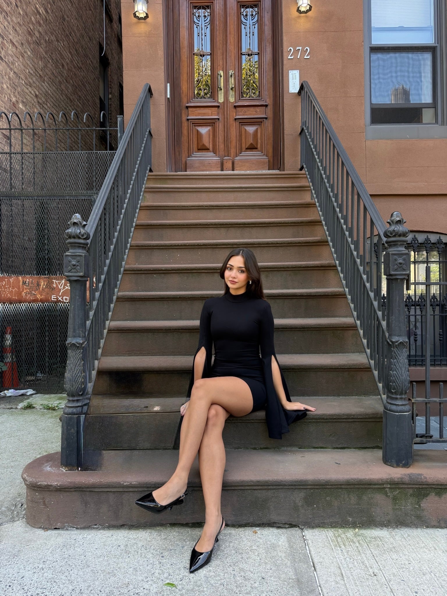 Woman in a black dress sitting on steps in front of a brownstone building.
