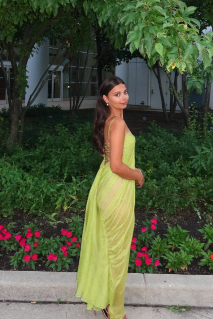 Woman in a green dress standing in a garden with trees and flowers.