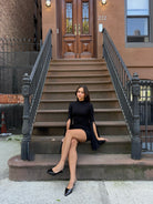 Woman in a black dress sitting on steps in front of a brownstone building.