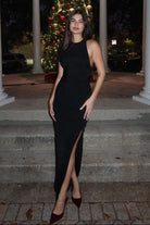 Woman in a black dress standing on steps with a decorated Christmas tree in the background.