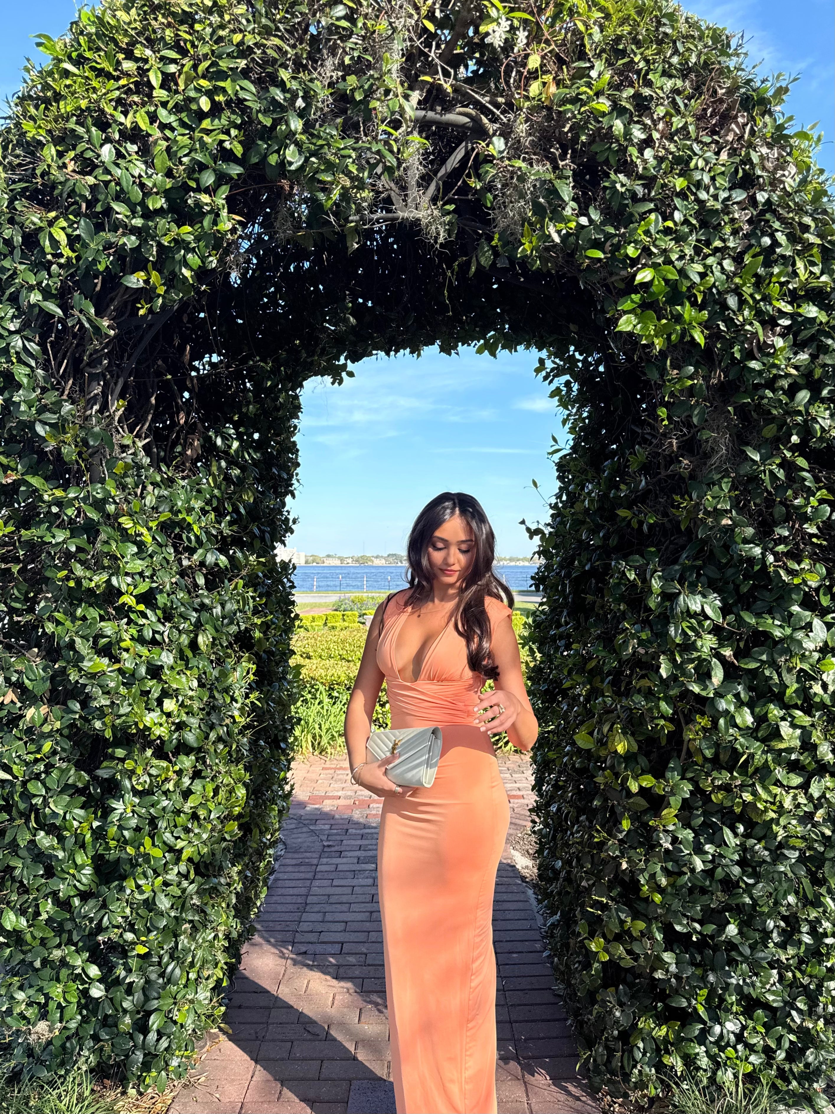 Woman in a peach dress standing in front of a green archway with a scenic background