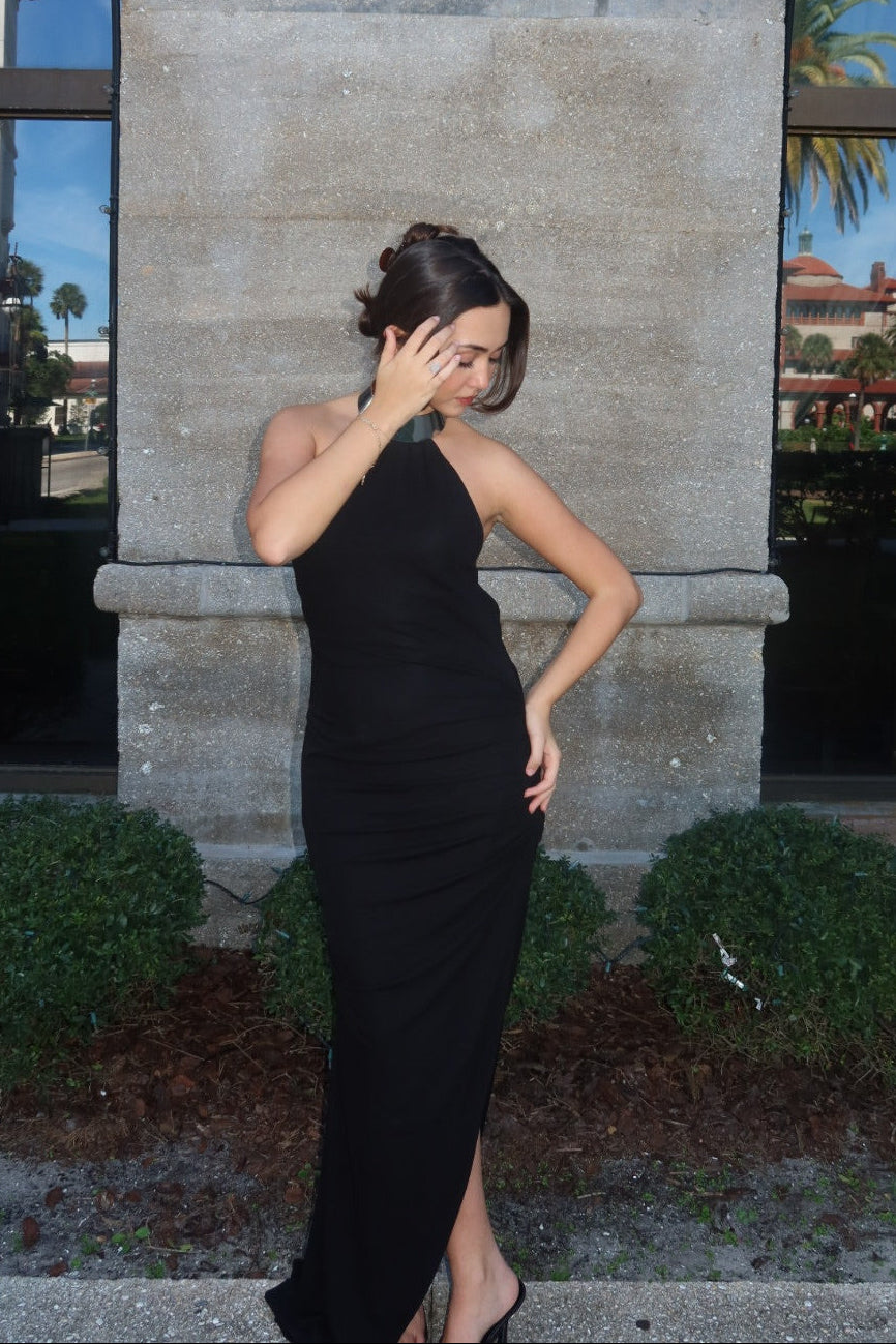 Woman in a black dress standing in front of a stone building with large windows.
