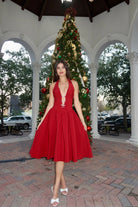 Woman in a red dress standing in front of a decorated Christmas tree under an open-air pavilion.
