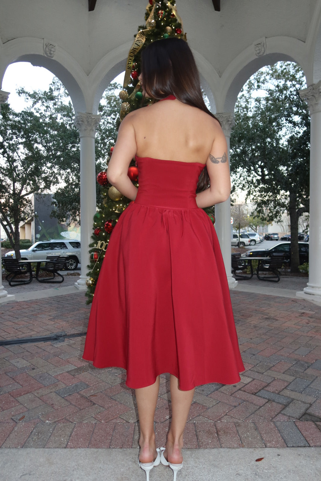 Person wearing a red dress standing in front of a decorated Christmas tree.