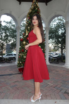 Woman in a red dress standing next to a decorated Christmas tree outdoors.