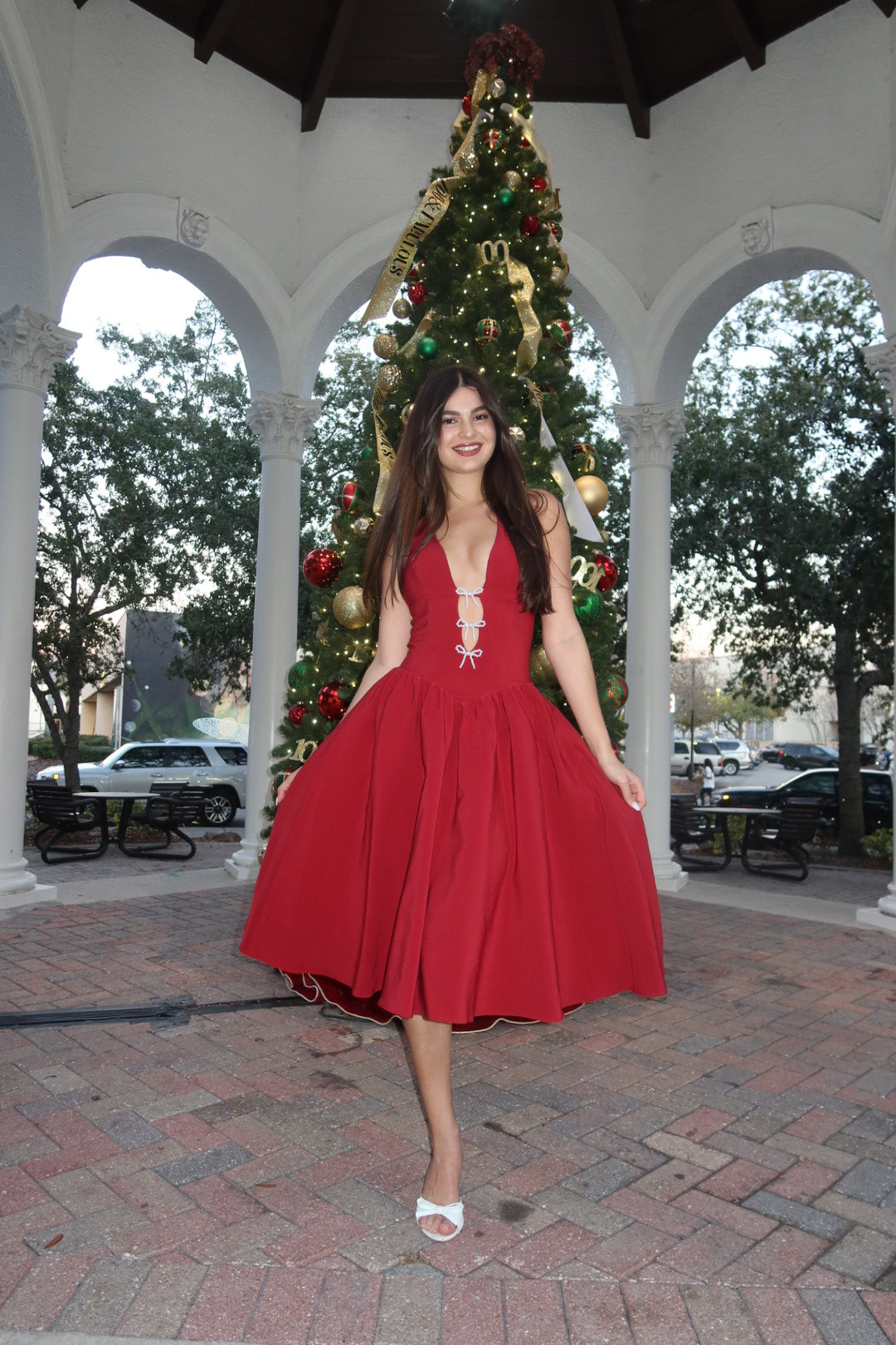 Woman in a red dress standing in front of a Christmas tree outdoors.